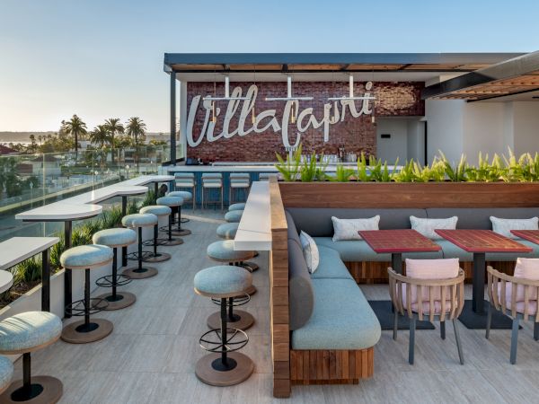 Rooftop terrace with stylish seating, tables, and a sign reading "Villa Capri." Scenic views and greenery create a welcoming atmosphere.