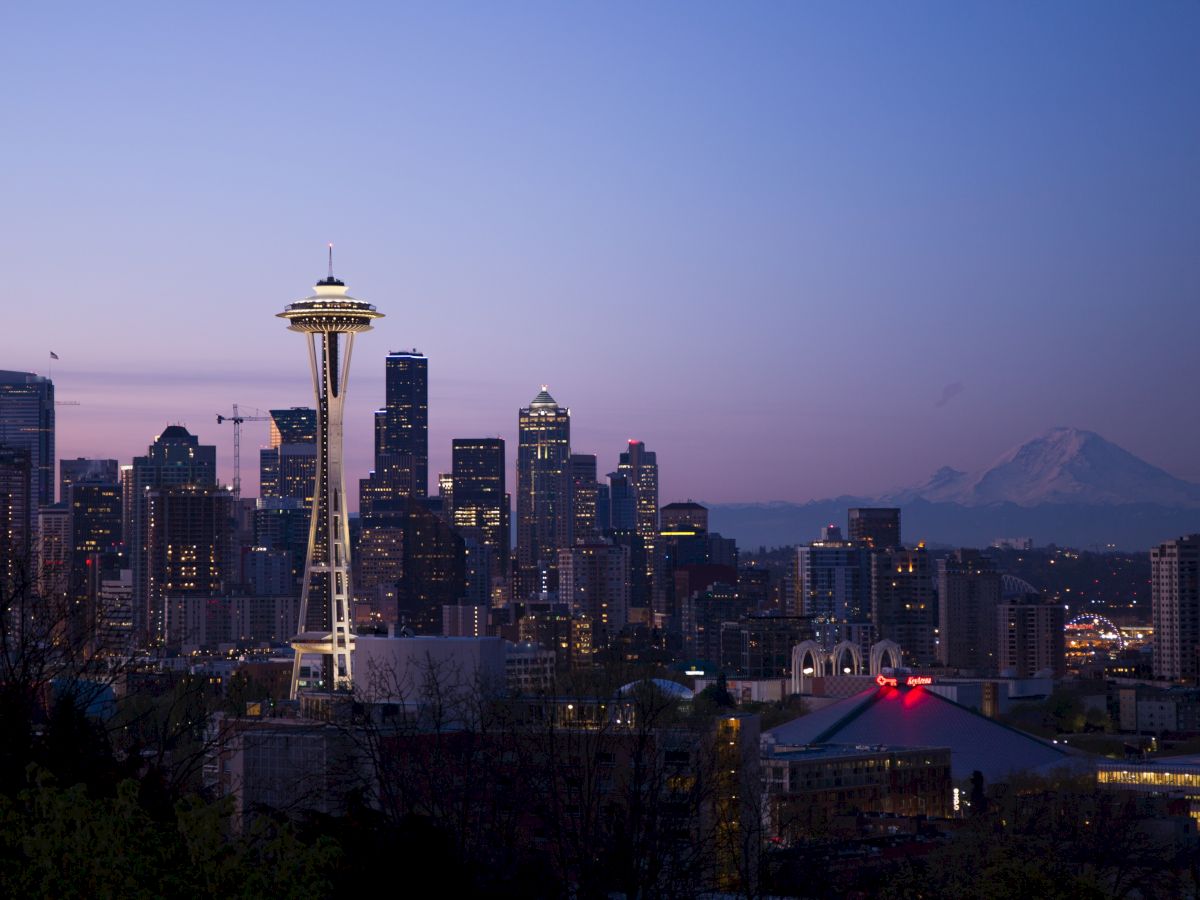 A city skyline at dusk with a prominent tower, surrounding buildings, and a mountain in the background under a purple sky.